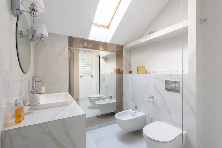 Moderne bad med marmorvegger, takvindu, servant, toalett og bidet. Lys og stilren innredning.
