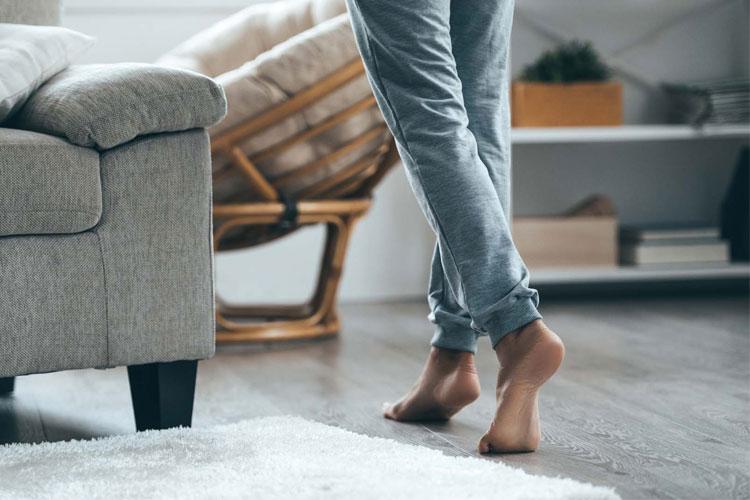 En person står barføtt på et teppe i stuen, ved siden av en sofa og en gyngestol.
