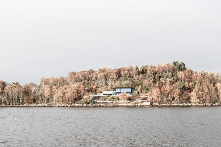 En moderne bygning på en ås med høstfargede trær ved en innsjø.