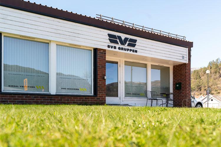 Kontorbygning med navnet "SVS Grupper" på fasaden, plassert på en grønn plen under klar himmel.