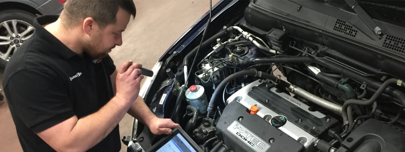 Mekaniker som bruker en datamaskin for å diagnostisere motorproblemer i en bil.