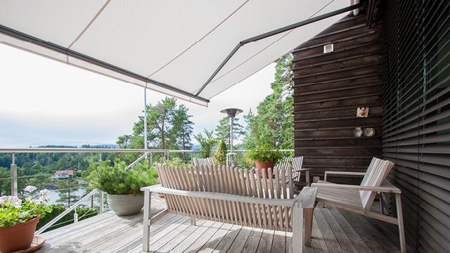 En moderne terrasse med en solskjerm, utemøbler og planter, med utsikt over landskapet.