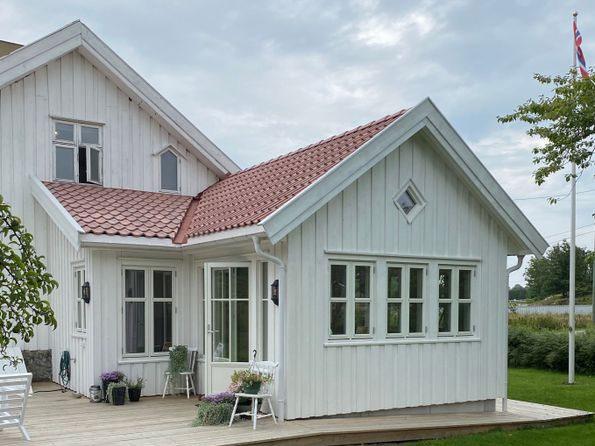 Hvit enebolig med rød takstein, veranda og store vinduer i et landlig miljø.
