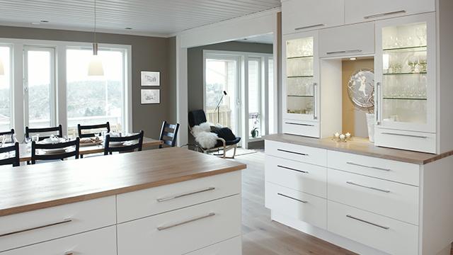 Moderne kjøkken med hvite skap, trebenkeplate og åpen stue med spisebord og stoler i bakgrunnen.