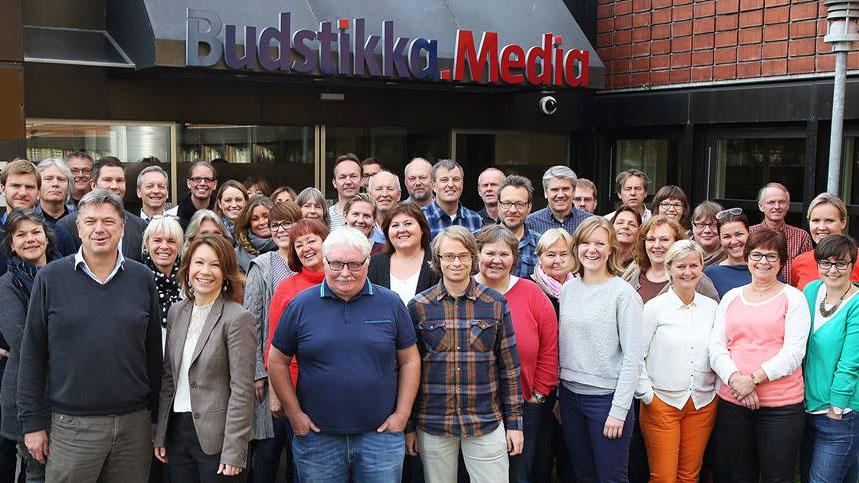 En gruppe ansatte fra Budstikka Media poserer foran bygningen, smilende og samlet for et gruppebilde.