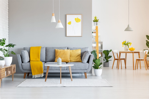 Moderne stue med grå sofa, gule puter, planter, og spisebord med stoler i lyst interiør.
