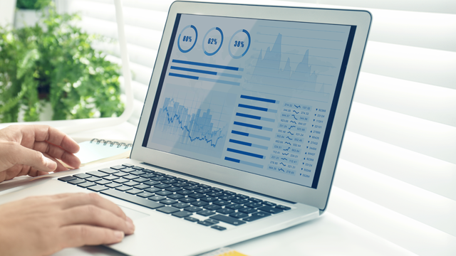 En person som bruker en laptop med grafiske data og diagrammer på skjermen, omgitt av grønne planter.