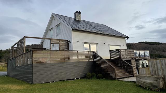 Moderne enebolig med terrasse og trapp, omgitt av natur i bakgrunnen.