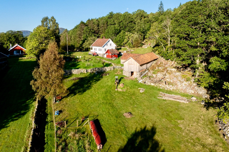 En oversiktsbilde av en gård med hus, låve og grønne områder omringet av trær.