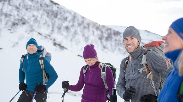 Fire personer i vinterklær smiler og står på snødekt fjell, klare for å gå på ski.