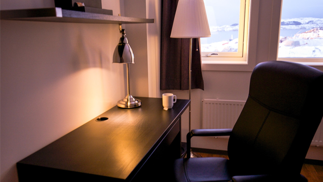 Moderne skrivebord med lampe, stol og kopp, med vindu som viser snødekte fjell i bakgrunnen.