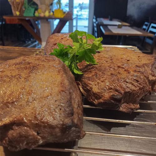 Tre saftige biter av stekt kjøtt med frisk persille på en rist, med en restaurantbakgrunn.