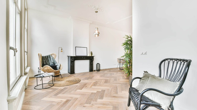 Lyst og moderne rom med parkettgulv, stoler, planter og en peis i en stilren innredning.