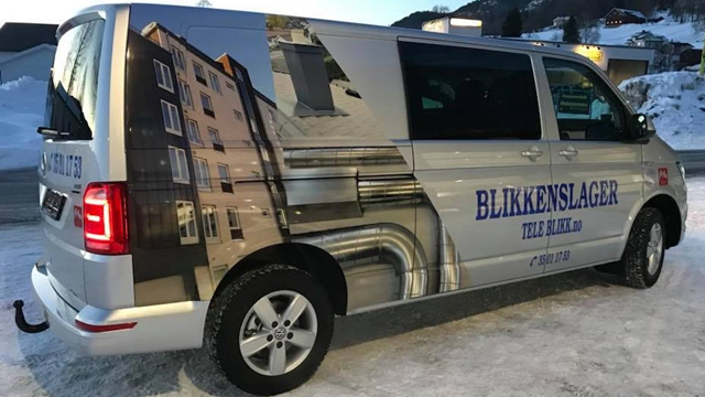 En varebil med reklame for blikkenslager, med bilder av bygninger og rør på siden, parkert i snøen.