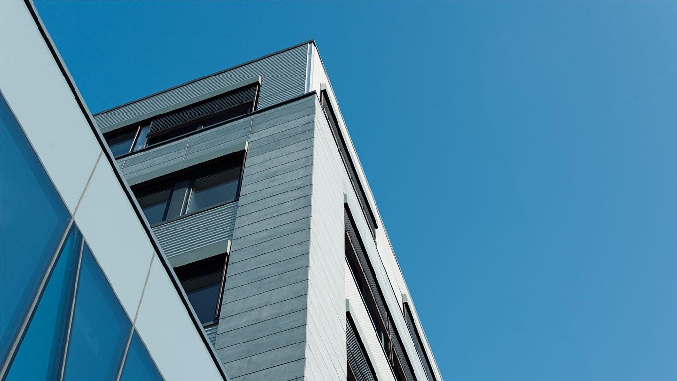 Moderne bygning med glassfasade og metallpanel under en klar blå himmel.