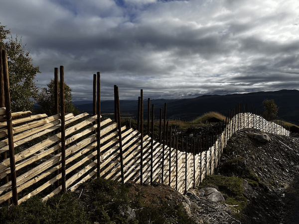 En bølgende gjerde laget av treplanker og stenger, med en dramatisk himmel i bakgrunnen.