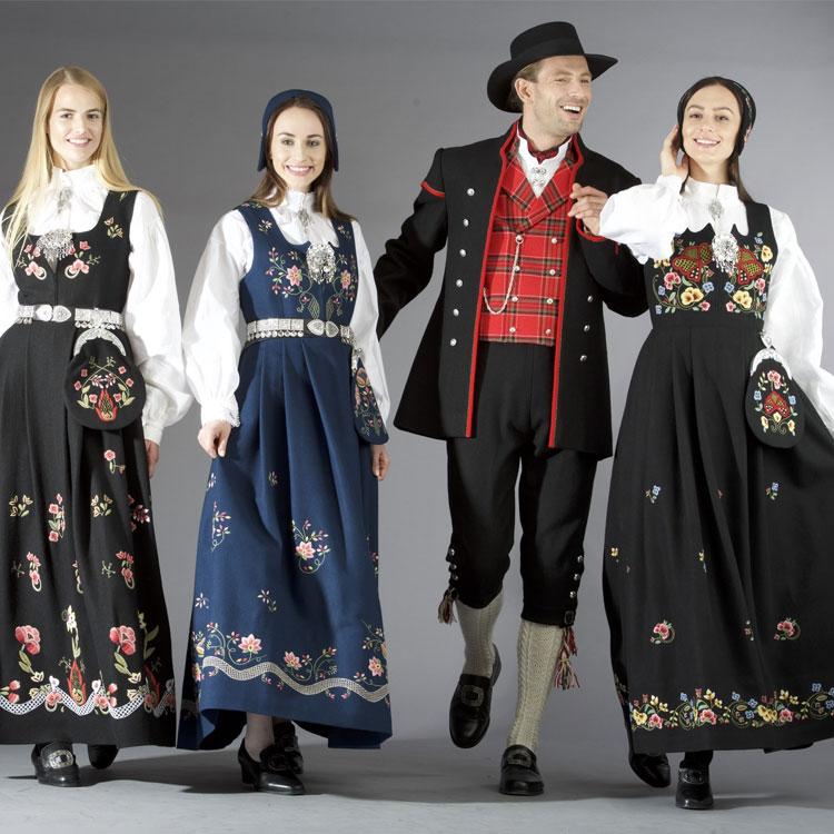 Fire personer i tradisjonelle norske bunader, med blomsterdekorasjoner og en mann i festdrakt.