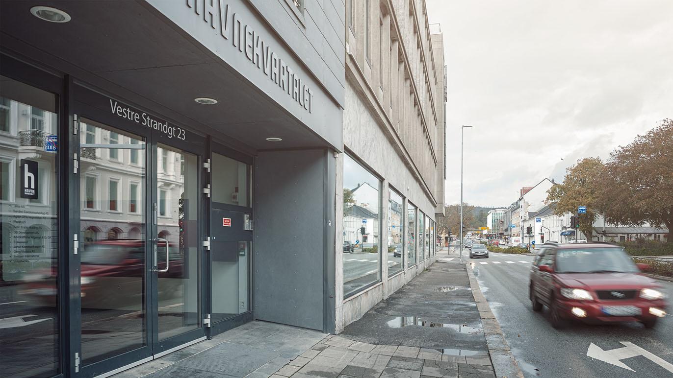 Inngangen til et moderne kontorbygg med vinduer og en bil som kjører forbi på gaten.