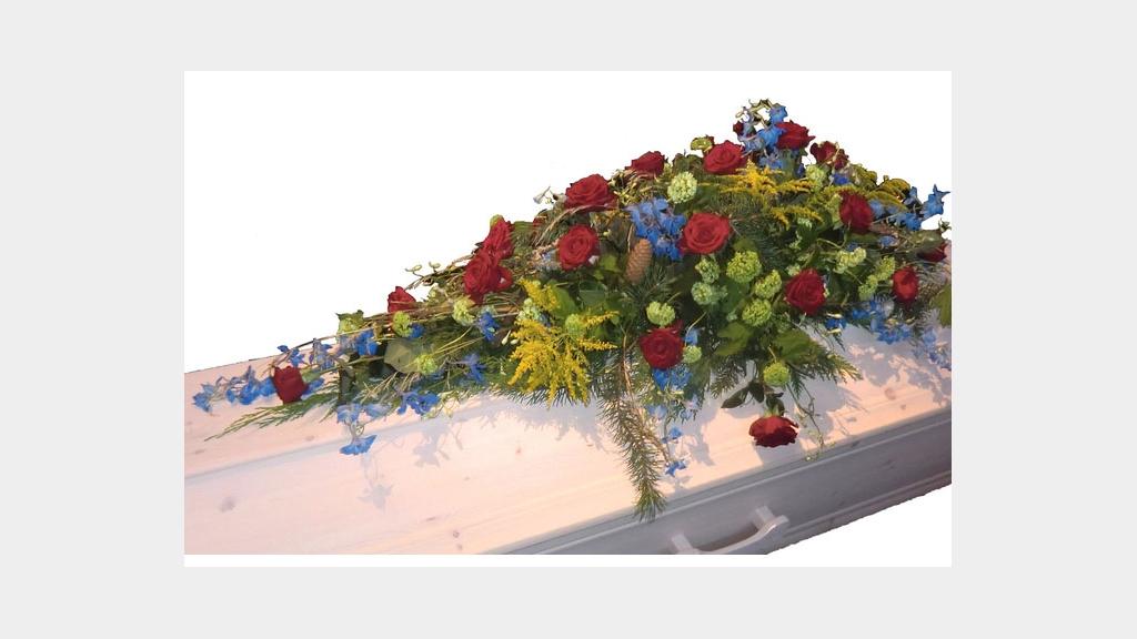 Blomsterdekorasjon med røde roser og blå blomster på en hvit kiste.