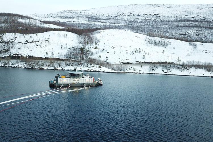 En båt som seiler på en rolig innsjø med snødekte fjell i bakgrunnen.