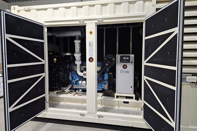 En åpen container med en motor og utstyr for strømproduksjon, plassert i et industrielt miljø.