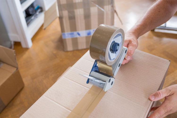 En person bruker tape for å lukke en pappeske i et rom med flere esker.