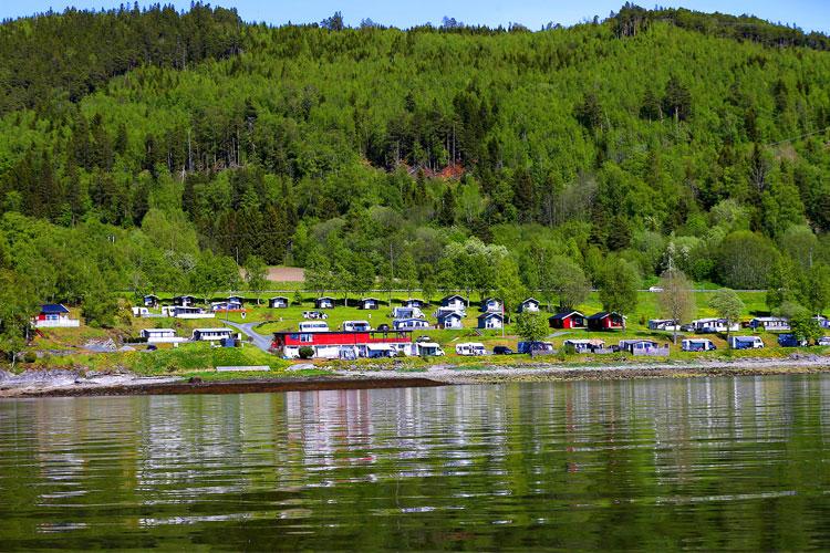 Utsikt over en campingplass med hytter og grønne trær langs en innsjø i Norge.