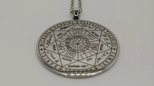 Et sølvmedaljong med mystiske symboler og inskripsjoner, hengende fra en kjede.