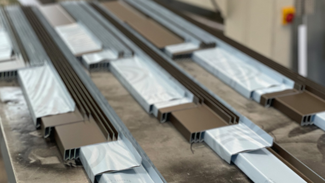 Ferdigbehandlede aluminiumsprofiler i brune og lyse farger på en produksjonslinje.