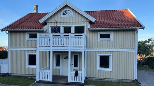 En lys gul enebolig med rød takstein, balkong og hvite detaljer, beliggende i et rolig nabolag.
