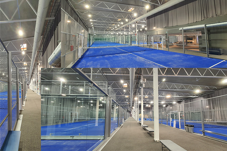 Innendørs sportsanlegg med blå baner, glassvegger og benker langs sidene. God belysning og moderne design.
