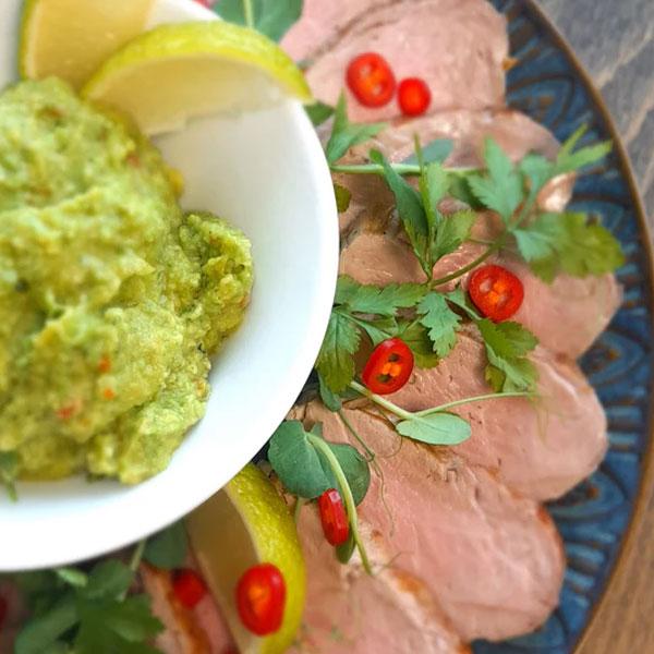 Skiver av kjøtt servert med guacamole, sitronbåter, chili og frisk persille på en dekorativ tallerken.