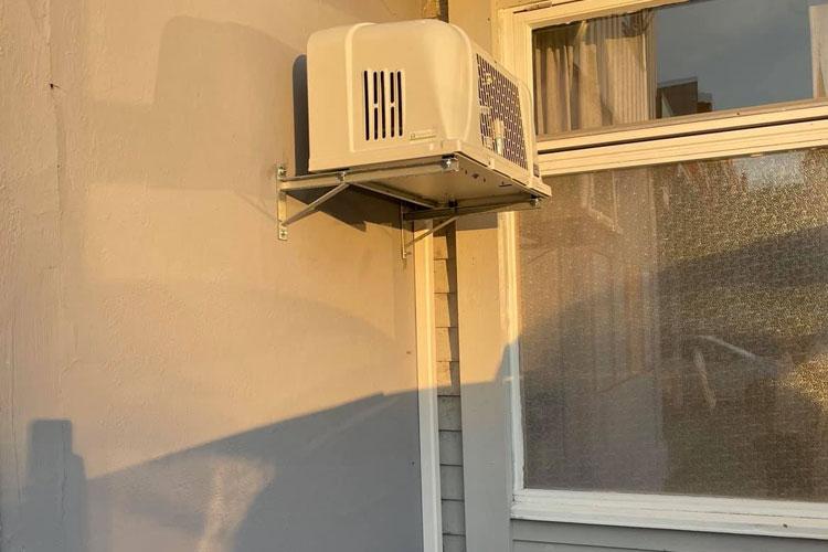 Klimaanlegg montert på veggen av et hus, med sollys som skinner på en grå overflate.