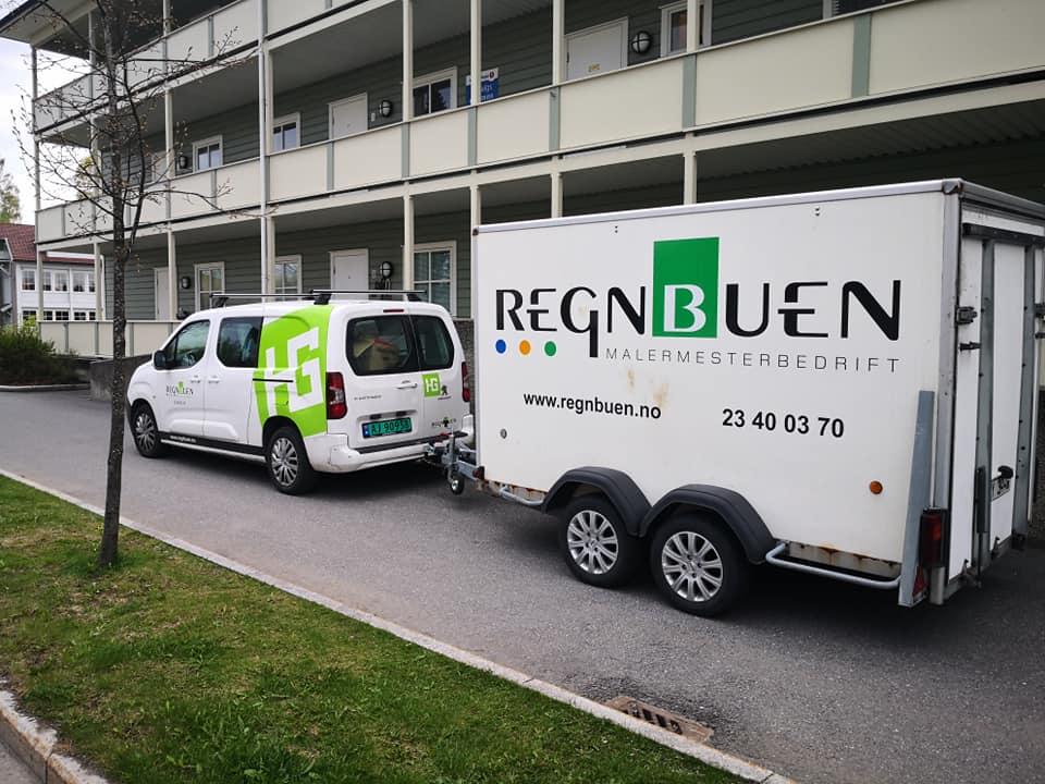 Bilde av en hvit varebil og en tilhenger med logoen til Regnbuen, parkert foran en bygning.