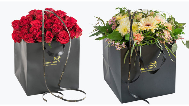 To vakre blomsteroppsatser i svarte gaveesker, en med røde roser og en med gule gerberaer.