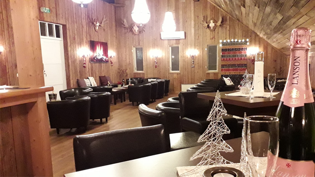 Koselig interiør i en restaurant med trevegger, komfortable stoler, lys og champagneflaske på bordet.