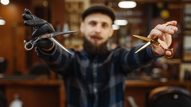 En barberer med skjegg holder to forskjellige frisørsaks i en frisørsalong.