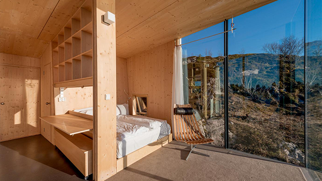 Moderne soverom med trevegger, stor vindu med utsikt over naturen og minimalistisk møblering.