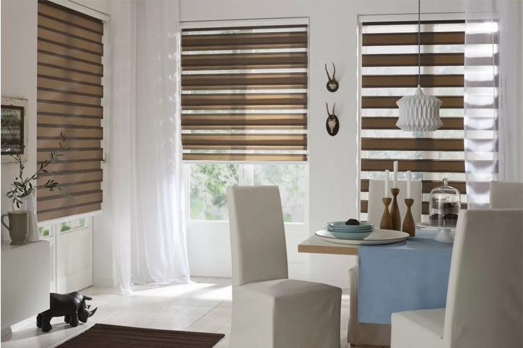 Moderne stue med brune persienner, hvite møbler og et spisebord dekket med tallerkener og glass.