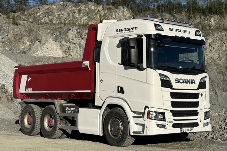 En hvit Scania lastebil med rød tippkasse står på en steinbruddplass.