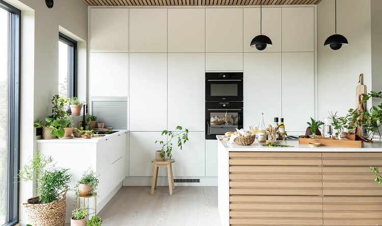 Moderne kjøkken med hvite skap, trepanel, planter og en kjøkkenøy med stoler og matlagingstilbehør.