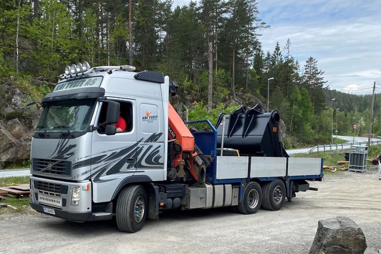 En stor lastebil med en kran og en container står parkert langs en vei i skogen.