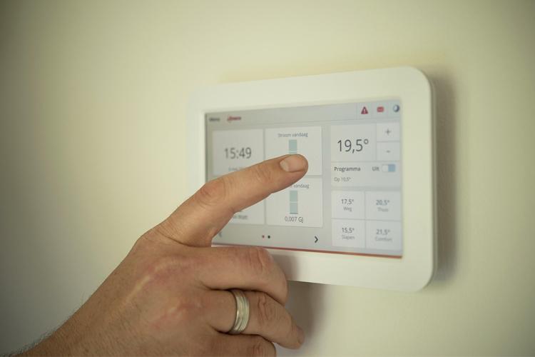 En hånd justerer temperaturen på en moderne termostat med digital skjerm.