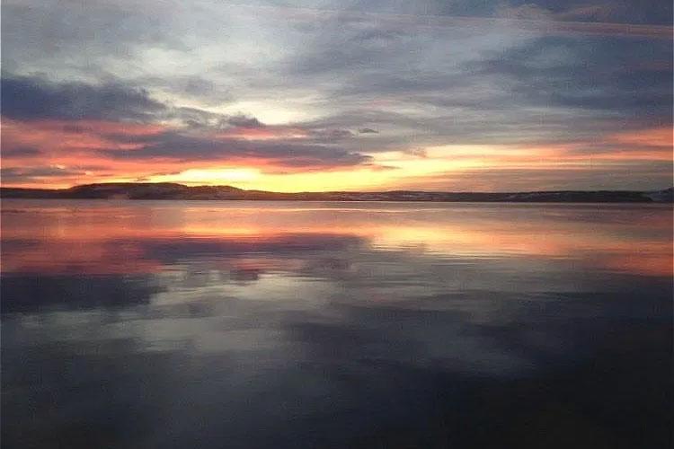 En vakker solnedgang over en rolig innsjø med reflekterende farger i himmelen.