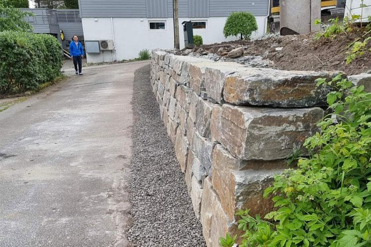 En steinmur langs en grusvei med en person som går forbi i bakgrunnen.