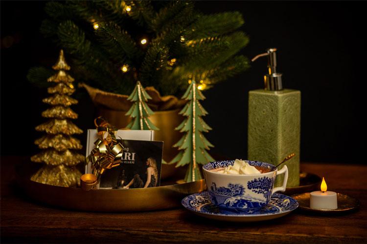 En koselig juledekorasjon med et juletre, lys, en kopp med krem, og en telysholder på et bord.