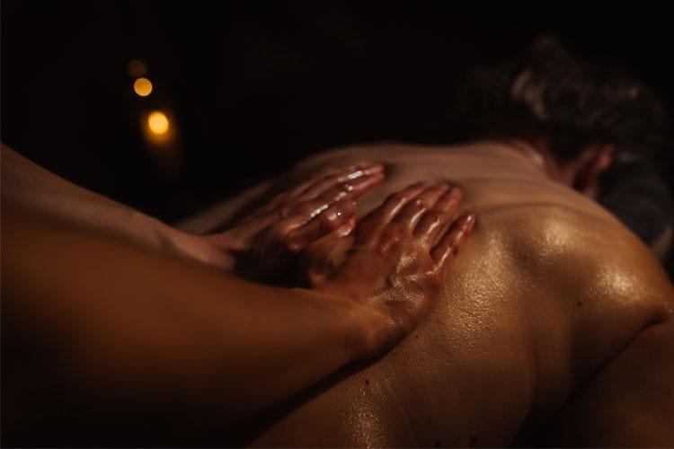 En person får massasje med olje, med fokus på ryggen og hender som masserer. Mørk bakgrunn og dempet belysning.