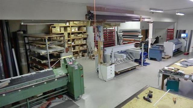 Verksted med maskiner, hyller med materialer og arbeidsbenker i et rom med god belysning.