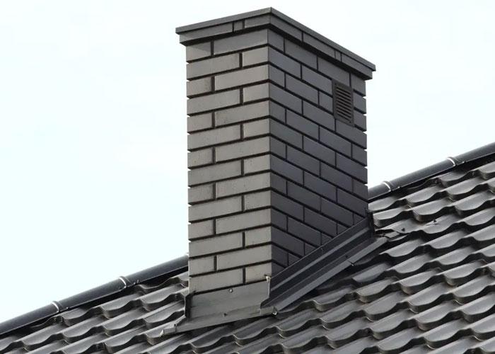 En mursteinpipe på taket av et hus med takstein.