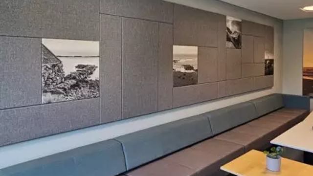 Bilde av en vegg med grå akustiske paneler og svart-hvite fotografier av landskap. Sofa og bord i forgrunnen.